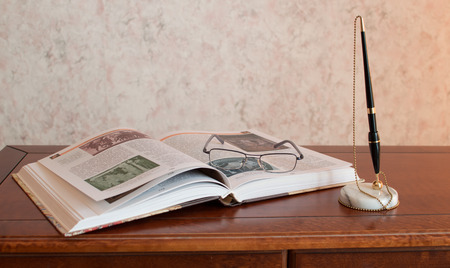 Pen, book and glasses on wooden deskの写真素材