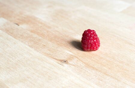 Single raspberry on wooden desk. Closeup composition. Natural light and shadows - light colors