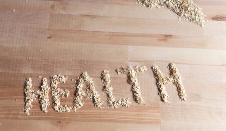 Oatmeal grains in form of word health on wooden desk. Bright and natural light and shadowsの写真素材