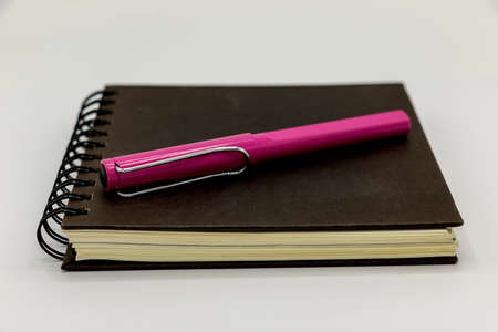 Notebook black color and pink pen white backgroundの写真素材