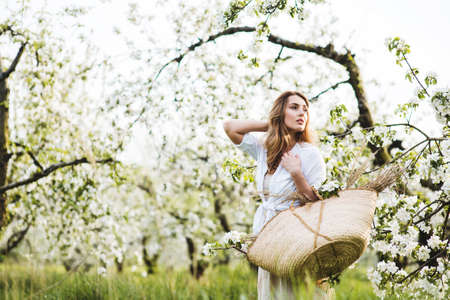 Beautiful young woman with a basket in blooming spring garden