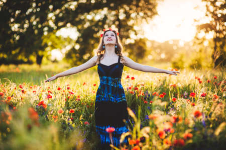 Beautiful young woman on the poppy field in sunlightの写真素材