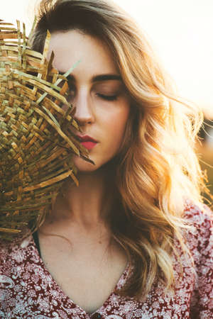 Portrait of beautiful young woman in field with a hat at summer sunset.の写真素材