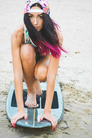 Beautiful sexy surfer girl with pink hair on the beach at sunset