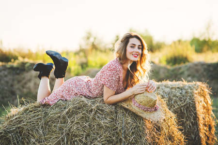 Beautiful young woman on a haystack at sunsetの写真素材