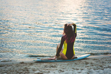 Beautiful sexy surfer girl with pink hair on the beach at sunsetの写真素材