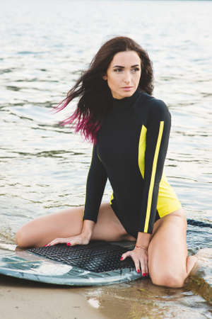 Beautiful sexy surfer girl with pink hair on the beach at sunsetの写真素材