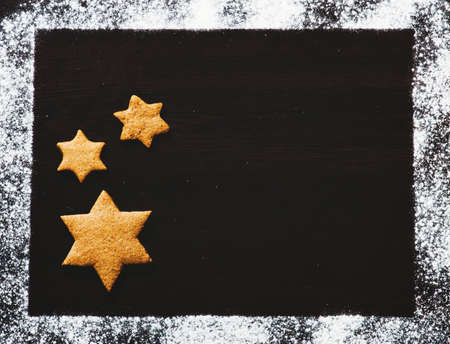 Traditional Christmas gingerbread cookies hanging over wooden background in a flour frame