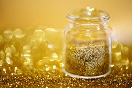 Gold glitter in a small bottle on golden background. Winter holidays concept.の写真素材