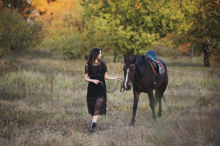 Adorable young woman walking with her horse in autumn forestの写真素材
