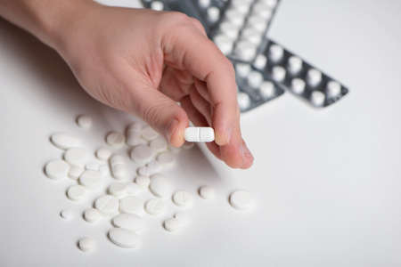 Hand holding a pill between thumb and forefinger on white backgroundの写真素材