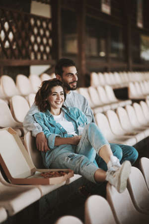 Smiling couple sitting together on empty sports tribuneの写真素材