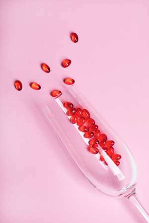 Red pills inside the wine glass on pink background