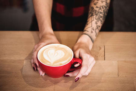 Top view of woman hands holding red mug of hot coffee standing on wooden table