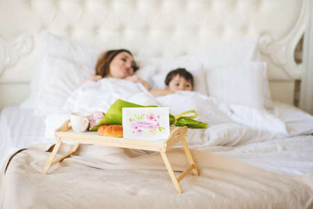 Young mother with her little son relaxing in the bed. Mothers Day concept. Greeting card and...