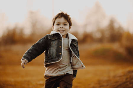 Happy young boy smiling and running on grass on autumn field.の写真素材