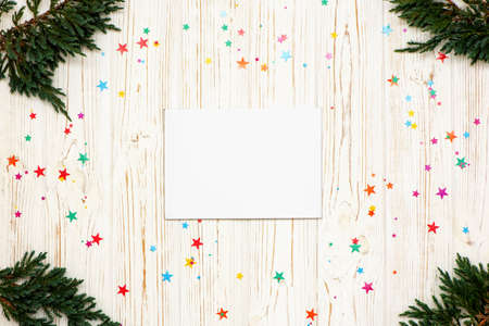 Christmas composition with paper blank, christmas tree branches and little colorful stars on white...