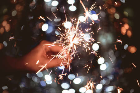 Toned image of hand holding a burning sparkler firework on light bokeh background.の写真素材