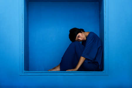 Young beautiful woman sitting in niche on blue background.の写真素材