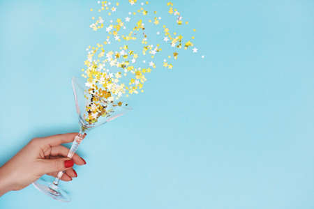 Woman hand holding martini glass with pouring out golden stars confetti on blue background.の写真素材