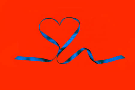 Blue ribbon in shape of heart on red background. Mockup for your text.の写真素材