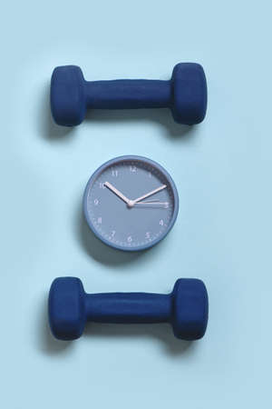 Clock and pair of dumbbells on blue pastel background. Time for sport concept.の写真素材