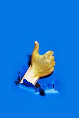 Hand with golden glitter break through the paper with the thumb up.の写真素材