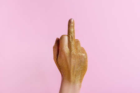 Woman hand with golden glitter gesturing with middle finger hole on pink background.の写真素材