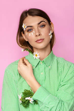 Portrait of young woman with flowers on her face on pink background.