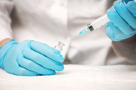 Doctor or nurse hands in blue gloves holding syringe and vaccine injection.
