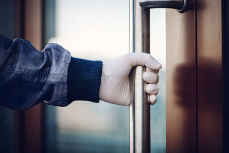 Hand in white latex glove holds handle while opening door. The concept of self-isolation during a pandemic and epidemic.の写真素材