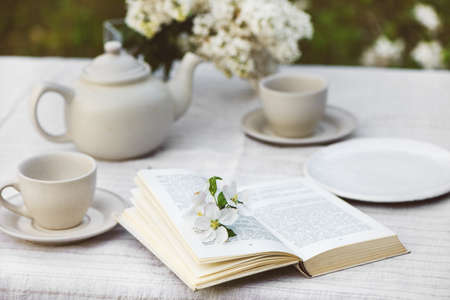 Romantic image with open book with flowers, tea cups, tea pot and branch of lilac.の写真素材