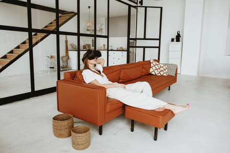 Beautiful young woman sitting on sofa at home wearing virtual reality headset.の写真素材