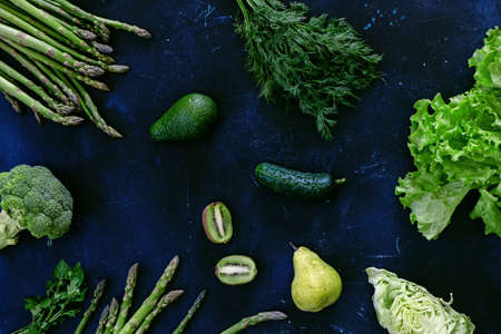 Fresh green fruits and vegetables on blue background.