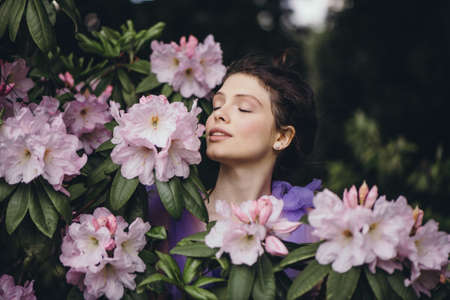 Beautiful young woman in blooming rhododendron bush.の写真素材