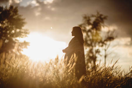 Silhouette of woman standing on meadow over sunset light.の写真素材
