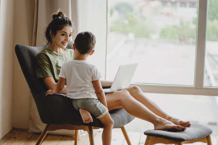 Mother and her son sit together on chair with laptop.の写真素材