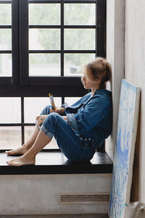 Young artist woman sitting on the windowsill.の写真素材