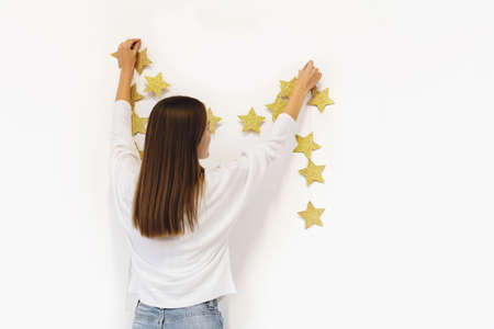 Long haired woman standing against a blank white wall holding festive garland decoration.の写真素材