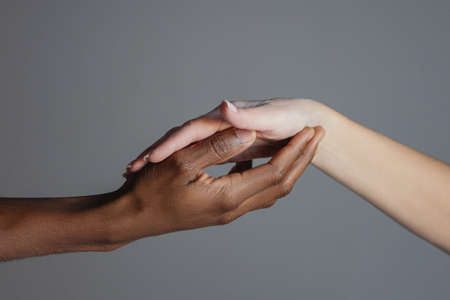 The black hand holds the white hand in its palm.の写真素材