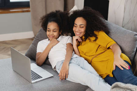 African american mother and her daughter using laptop lying on couch.の写真素材