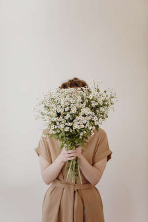 Woman hiding behind a bunch of daisies on white background.の写真素材
