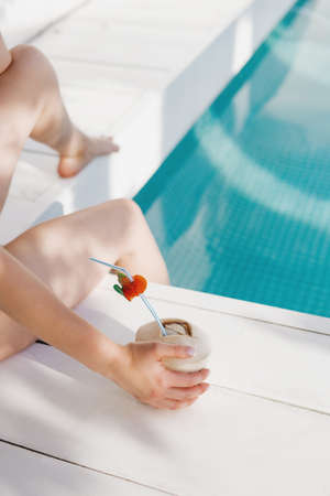 Cropped image of young woman holding fresh raw coconut in swimming pool.