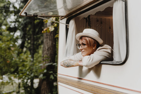 Pretty young woman looking through opening the camping van window in the morning.の写真素材