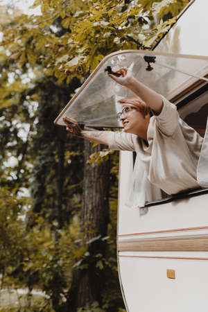 Young woman opening camping van window in the morning in autumn forest.の写真素材