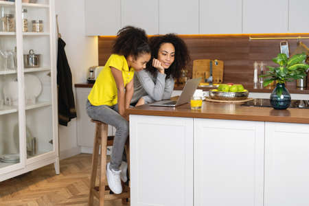 Mother and daughter using laptop together in kitchen.の写真素材