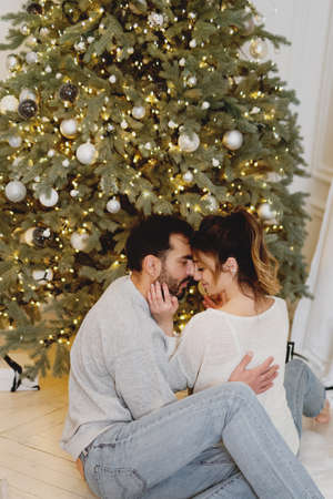 Young pretty couple kissing near Christmas tree at home.の写真素材