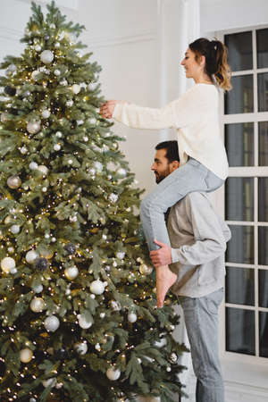Couple decorating Christmas tree. Woman sitting on the shoulders of man.の写真素材