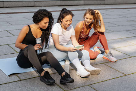 Three sporty women having fun and laughing looking smartphone after urban fitness workout.