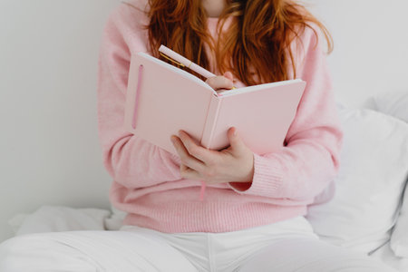 Cropped image of woman sitting on the bed and writing down in notebook.の写真素材